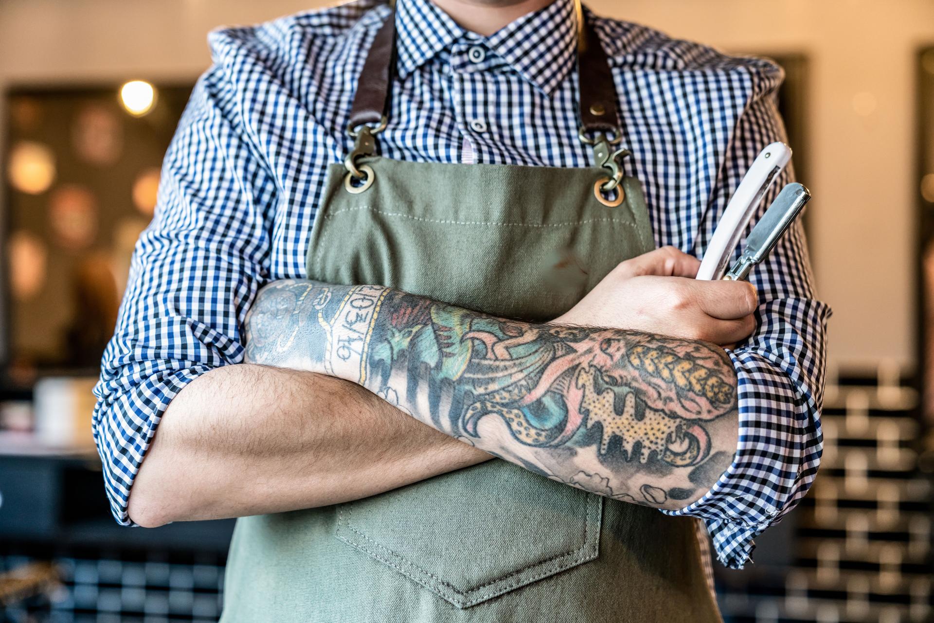 Unrecognizable barber with arms crossed holding a straight edge razor